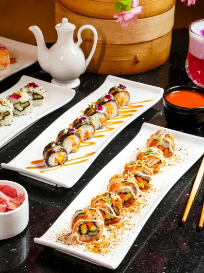 A long platter showcasing three different varieties of sushi rolls, elegantly garnished and sauced. The composition leads the eye across the frame, highlighting the variety and artistry of the dishes.