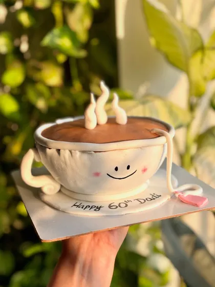 The full view of the adorable teacup-shaped cake, complete with a smiling face and steaming hot "tea" made of frosting.