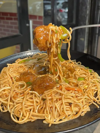 A close-up of a Manchurian ball and noodles on a fork. This dish is a favourite among my customers for its delicious taste.