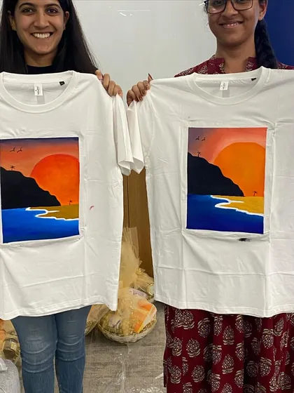 Two colleagues proudly displaying the beautiful sunset scenes they painted on t-shirts. It’s a wearable piece of art and a great memory from a fun team building activity.