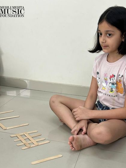 A young learner thoughtfully arranges popsicle sticks, demonstrating her understanding of rhythmic notation. These foundational skills are crucial for future musical development.