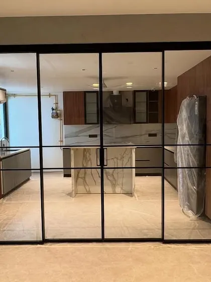 A handover day shot showing the new crittall-style sliding glass doors that separate the kitchen from the living area. The kitchen island is still wrapped, but the overall design is visible.