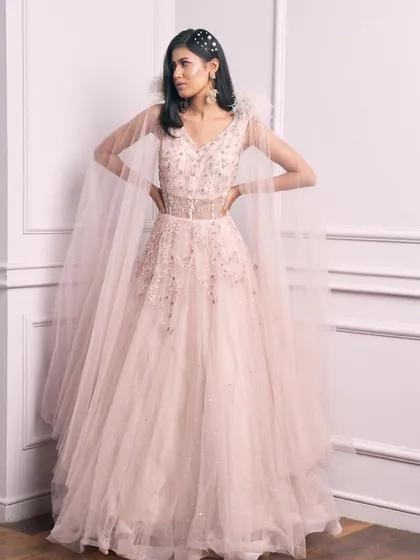 Live your own fairy tale in this Indo-western princess gown. The pale pink tulle, delicate embroidery, and feather-capped cape create a look that is pure magic.