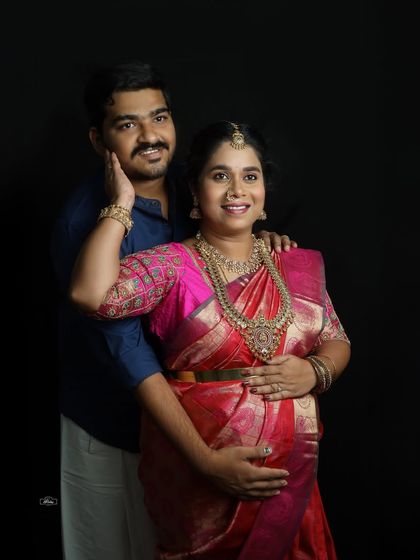 An elegant couple portrait against a simple black background. This style of traditional maternity photography puts all the focus on the couple's connection and the beauty of the silk saree.