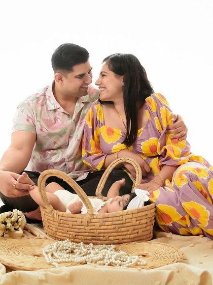 A candid and happy moment during a newborn session. The parents share a look of love while their baby rests in a wicker basket, set against a bright and airy backdrop.