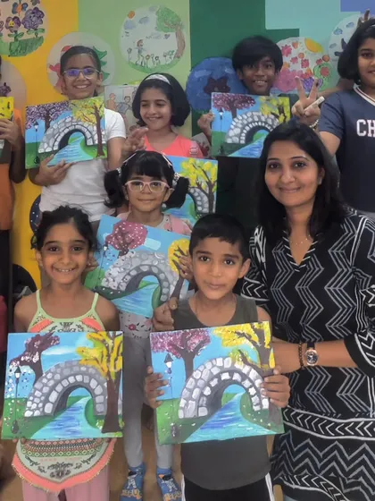 A happy group photo from a four-day acrylic painting workshop. I'm surrounded by my students, all proudly holding up their finished canvases featuring a charming stone bridge over a river.