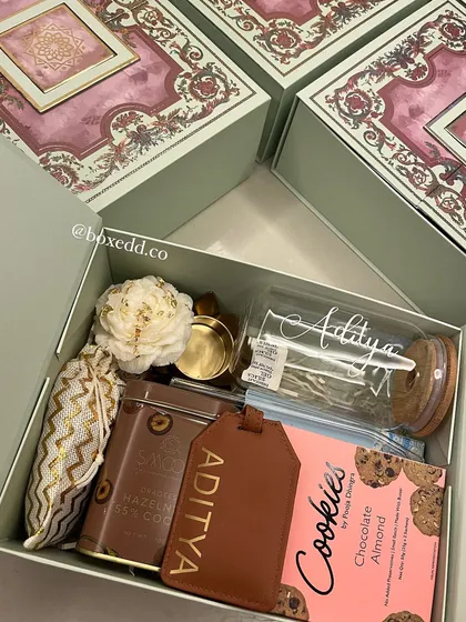 A close-up of a personalized hamper for "Aditya," featuring a custom-engraved glass and luggage tag, making the gift uniquely theirs.