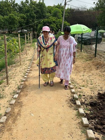 A senior citizen from Quota International walks with a cane along the path at our plantation site, her determination to contribute truly inspiring.