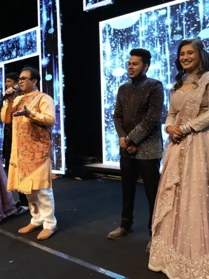 A wider shot of the stage, showing the couple and their family listening intently to Mr. Dilip Joshi.