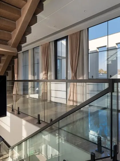 Looking down from the staircase landing, this view captures the double-height windows and the seamless flow of space. The glass railings ensure that views and light are unobstructed.