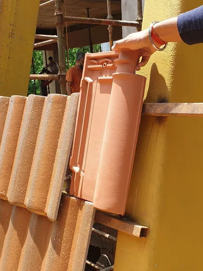 A craftsman demonstrates how the red mission tiles are interlocked and secured to the roof's framework. This precision is key to achieving the parabolic shape and ensuring structural resilience against heavy rains.