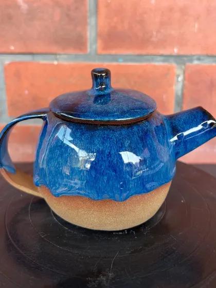 A wheel-thrown teapot with a dripping blue glaze over a raw stoneware base. This was part of a student's final collection.