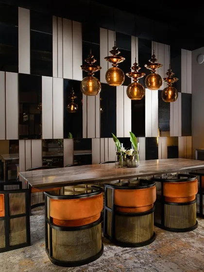This dining space is a study in contrasts. I combined leather, mirror, and metal strips for the wall panelling to create a bold, graphic effect. The vibrant orange velvet chairs and stone-top table complete this energetic and luxurious setting.