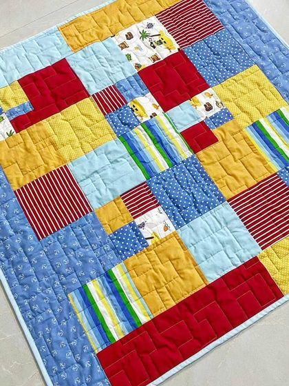 An angled shot of a bright and cheerful baby quilt, featuring a playful mix of primary colors and simple geometric blocks.
