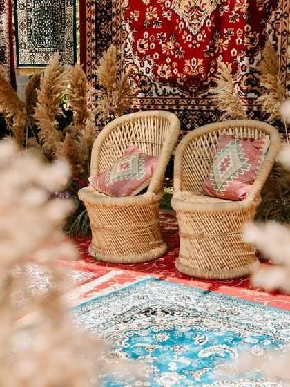 An artistic shot of the Haldi seating area, with rustic wicker chairs and colorful cushions framed by soft pampas grass, perfectly capturing the boho aesthetic.
