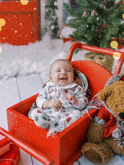 Baby's first Christmas. This little one is all smiles in a red sleigh, creating a memory that will be cherished forever.