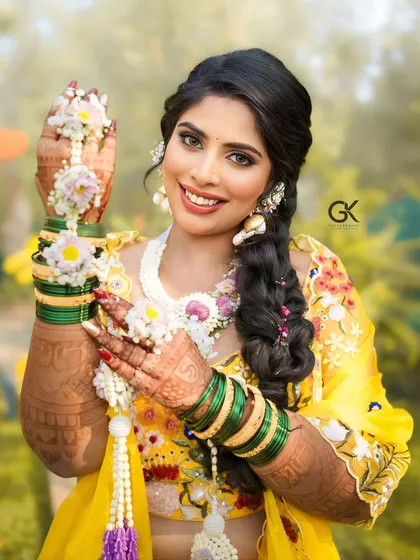 A close-up of a smiling bride, showing off her intricate floral hathphool and maang tikka.