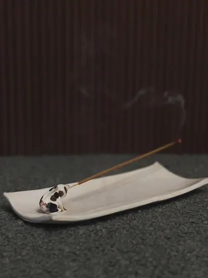 A minimalist incense holder featuring a tiny, spotted dog. The simple, elegant design allows the focus to be on the whimsical animal figure.