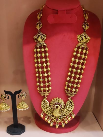 A beautiful antique-finish haram with a peacock pendant and red bead detailing, paired with matching jhumkas.