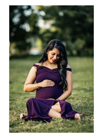A relaxed and happy portrait of a mother-to-be sitting barefoot in the grass, smiling down at her belly. This image feels natural and full of warmth.