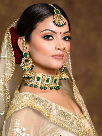 A classic bridal portrait. This look features a neutral makeup palette with defined eyes, paired with a stunning green and gold jewelry set.