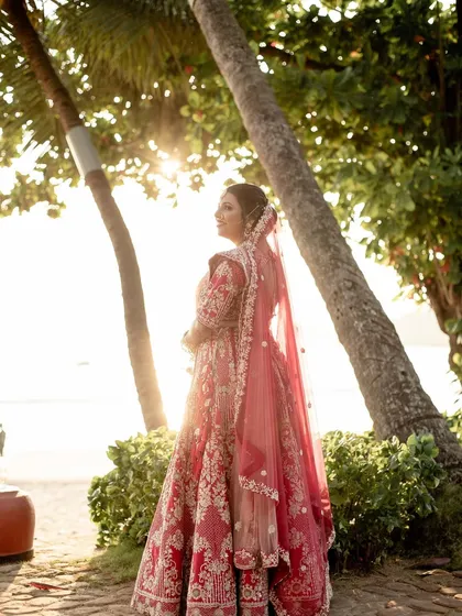 A stunning shot of the bride against the setting sun. The warm light enhances her glowing makeup and the rich color of her traditional red lehenga.