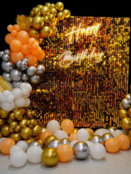 A glamorous birthday backdrop with a gold and orange sequin wall. The balloon arrangement in gold, silver, orange, and white adds a burst of color and fun.
