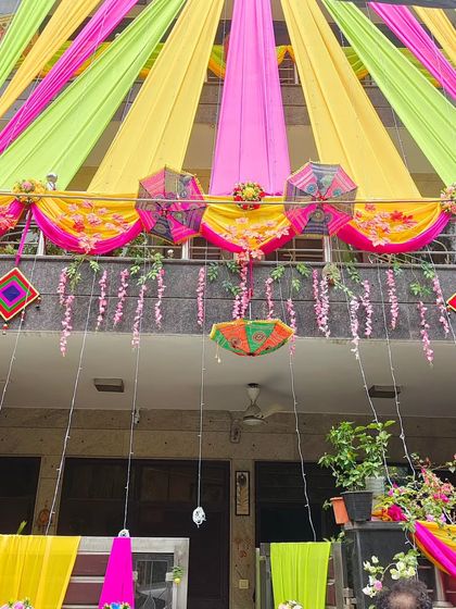 A closer look at the balcony and entrance decoration, featuring pink and yellow drapes, hanging flowers, and traditional umbrellas.