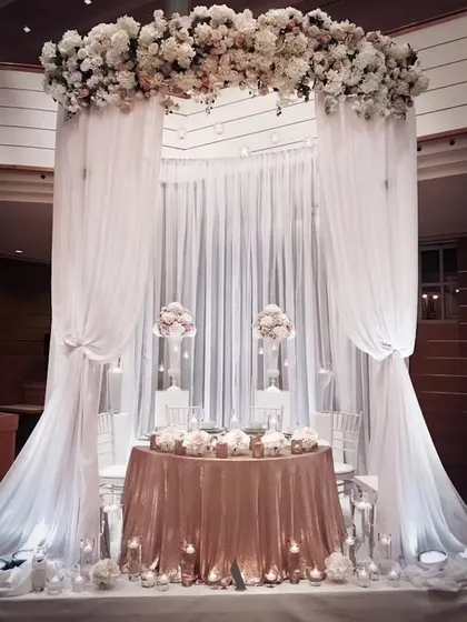 My work also includes timeless elegance for more formal events. This all-white decor for a ring ceremony or reception uses flowing drapes, a dense floral arch, and soft lighting to create a sophisticated and ethereal ambiance.