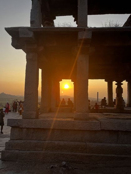 The sun sets through the stone pillars of a mandapa in Hampi. These structures were not just architectural marvels but also spaces for community, art, and spiritual practice, embodying the union of life and yoga.