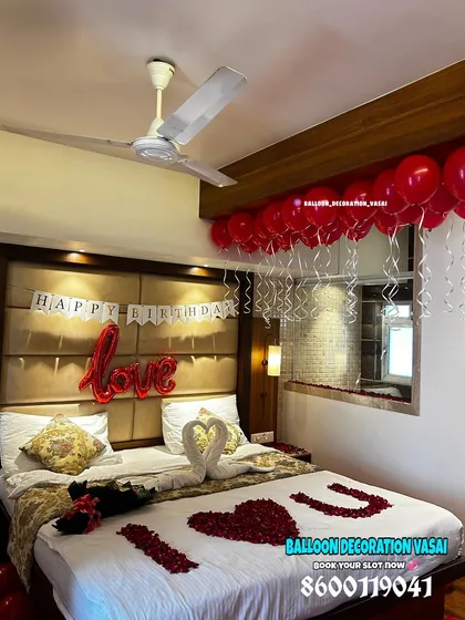 A simple yet beautiful birthday surprise setup in a hotel room. It includes a "Happy Birthday" banner, "love" foil balloon, and a bed decorated with rose petals and towel swans.