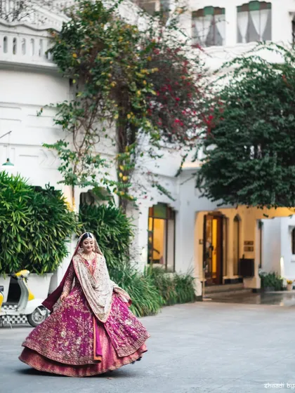 A wide shot of the bride in her royal magenta lehenga, capturing the grandeur of her outfit and the beautiful venue.