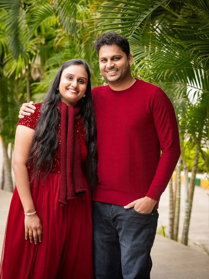 A classic couple's portrait taken outdoors. Their coordinated red outfits and the beautiful green background create a striking and romantic image.