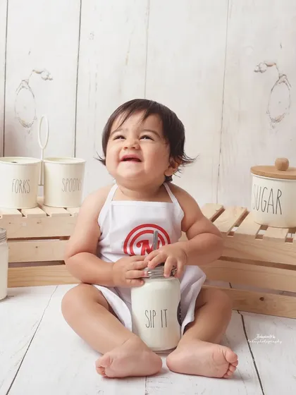 Our little chef is all smiles as he enjoys a jar of "milk." The rustic wooden props and vintage-style containers add to the charm of this delightful themed photoshoot.
