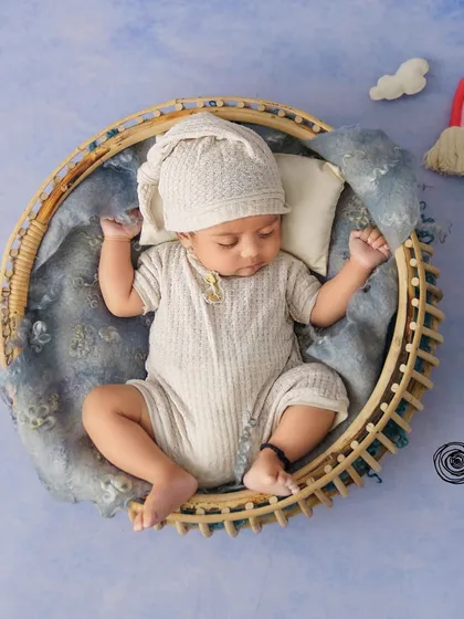 A cozy, round basket pose. The neutral tones and the simple rainbow and cloud props create a serene and dreamy atmosphere.