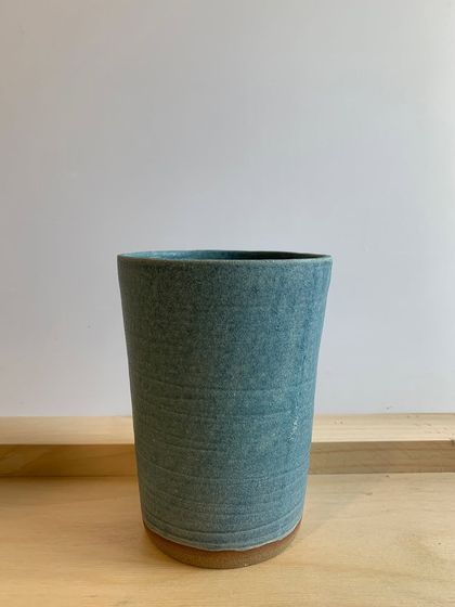 A tall, cylindrical vase with a textured, denim-blue glaze. The subtle lines from the wheel-throwing process are still visible, adding to its handmade charm.