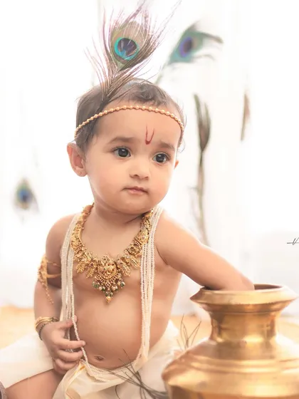 A simple yet powerful portrait. Against a clean, white background, the focus is entirely on the baby's innocent expression and the traditional Krishna styling.
