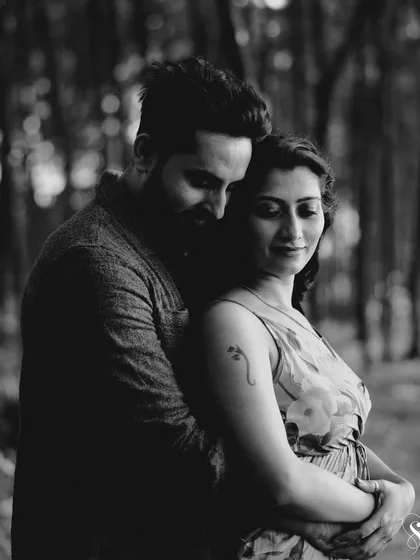 An intimate embrace captured in moody black and white. The soft focus and deep shadows of the forest create a sense of privacy and deep connection.
