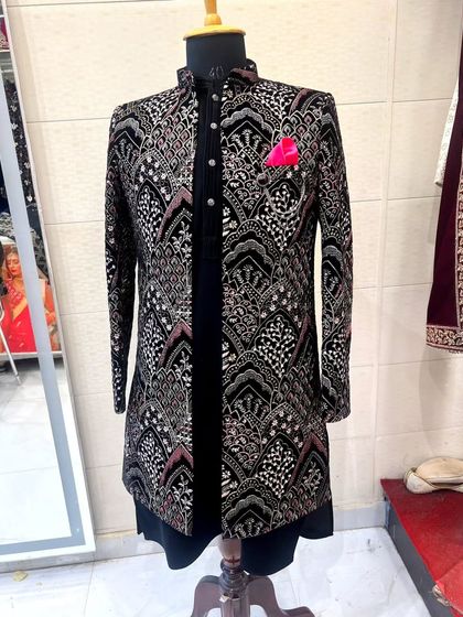 A black Indo-Western shrug set displayed on a mannequin. The jacket features a detailed, multi-colored pattern, perfect for layering over a simple kurta for a festive look.