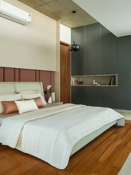 This bedroom showcases a refined material palette, with an upholstered headboard, dark wall paneling, and an exposed concrete ceiling. The design focuses on creating a comfortable and texturally rich private space.