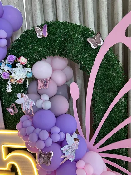 A detailed view of the fairy-themed decor, focusing on a large butterfly wing prop made of balloons and a faux-grass arch. This shot highlights the intricate combination of balloons, flowers, and fairy cutouts that create our enchanted forest look.