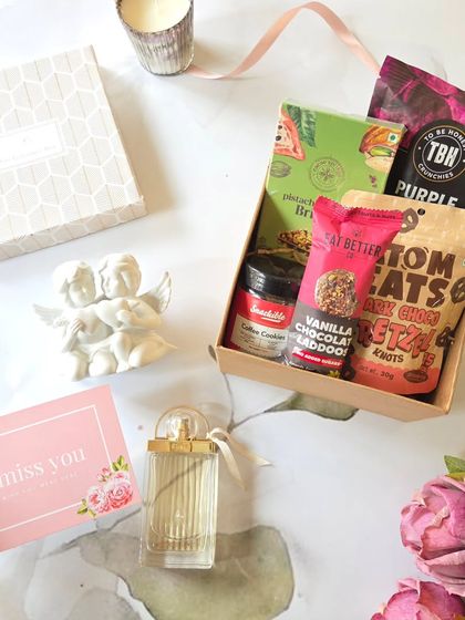 This romantic hamper is perfect for a cozy celebration. It features vanilla chocolate laddoos, pretzels, and a scented candle, paired with a perfume bottle and a sweet "I miss you" card.