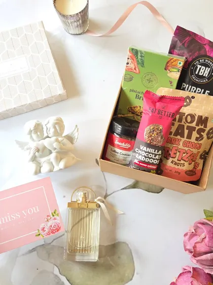 This romantic hamper is perfect for a cozy celebration. It features vanilla chocolate laddoos, pretzels, and a scented candle, paired with a perfume bottle and a sweet "I miss you" card.