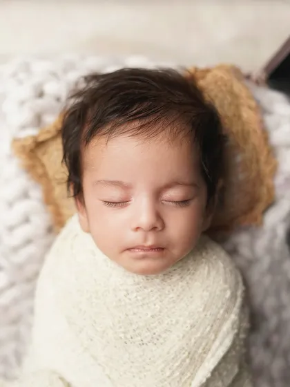 A close-up of a newborn's face as he sleeps peacefully in a vintage-style suitcase. This creative prop adds a touch of whimsy to the infant photoshoot.