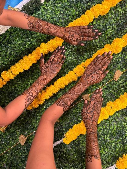 A creative shot of multiple hands displaying their detailed henna designs against a decorative backdrop.