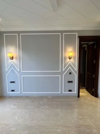 This bedroom features a sophisticated grey accent wall with classic moulding, complemented by warm wall sconces. The dark wooden door adds a touch of richness to the space.