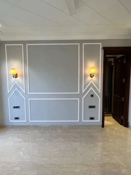 This bedroom features a sophisticated grey accent wall with classic moulding, complemented by warm wall sconces. The dark wooden door adds a touch of richness to the space.