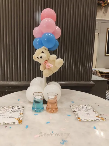 This teddy bear centerpiece is perfect for guest tables at a baby shower. The floating bear is carried by a bunch of pink and blue balloons, with themed stationery and confetti scattered on the table to complete the look.