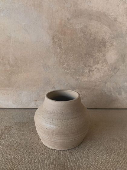A small, wheel-thrown vase in its raw state. The throwing lines are still visible, telling the story of its creation on the wheel.