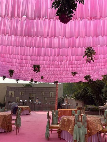 A view of the dining area under a canopy of bright pink fabric. This color theme creates a cheerful and celebratory atmosphere for a daytime wedding event.